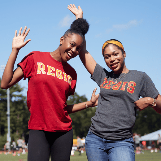 Regis students in Regis apparel waving to the camera on the Athletics field